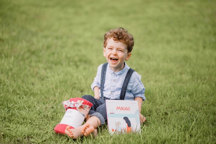 Boy laughing with a book and blanket on grass