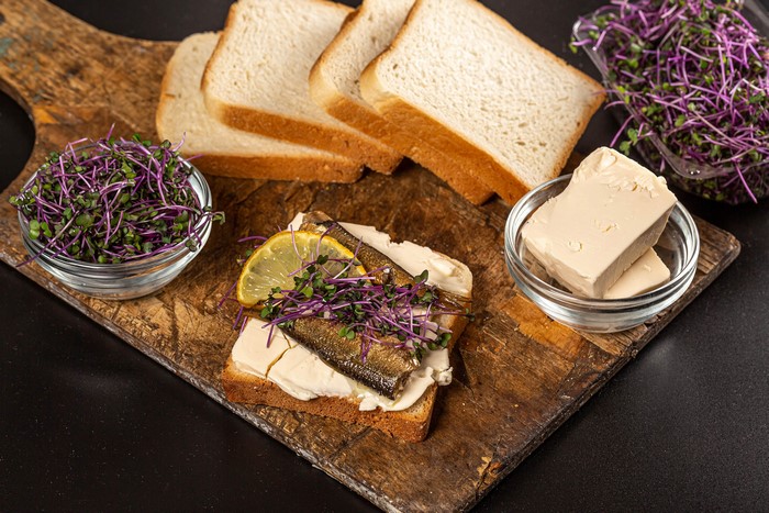 Sandwich with fish, microgreens, and butter on a cutting board