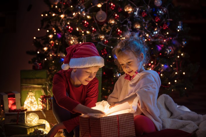 Children opening Christmas gifts by a tree