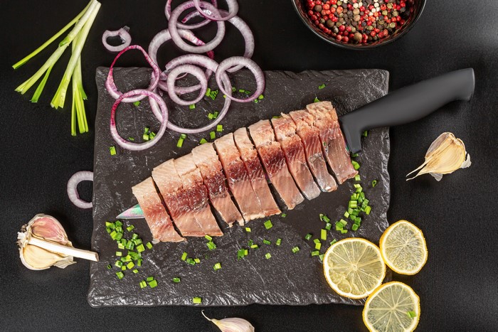 Sliced herring with onions, lemons, and garlic on a cutting board