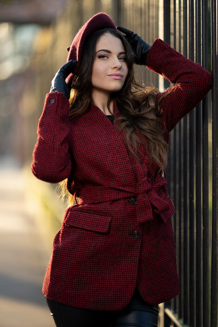 Woman in red coat and beret posing by fence
