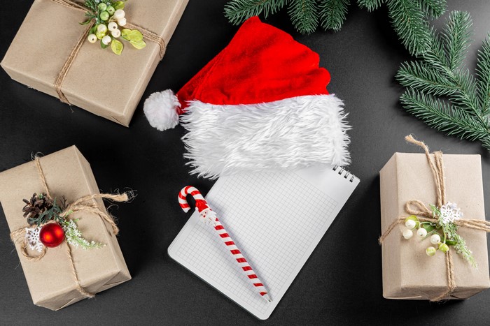 Christmas gifts, Santa hat, notepad, and pen on black background