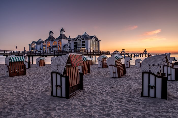 Beach chairs on sandy beach with pier at sunrise