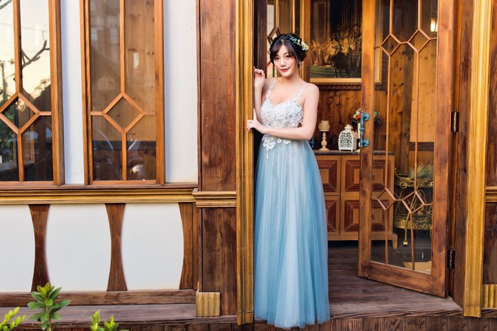 Asian woman in a blue dress posing by a wooden door