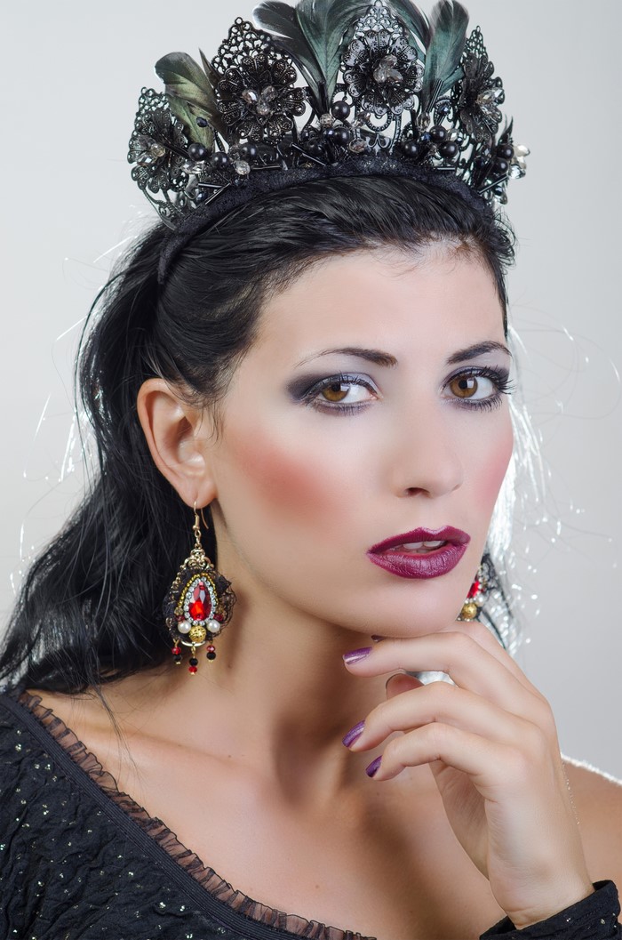Woman with dark hair and ornate crown and earrings