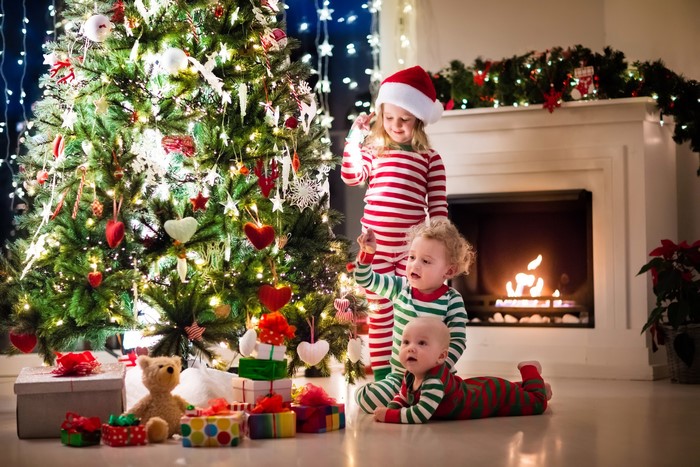 Children in pajamas by a Christmas tree and fireplace