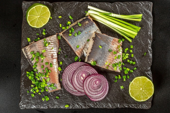 Herring fillets with red onion, lime, and scallions on a cutting board