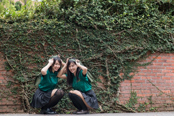 Two Asian schoolgirls in uniform crouching