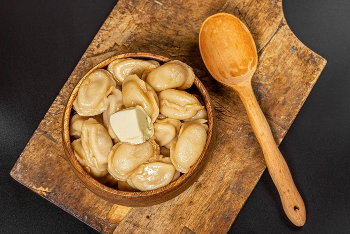 Pelmeni with butter on a cutting board with a spoon