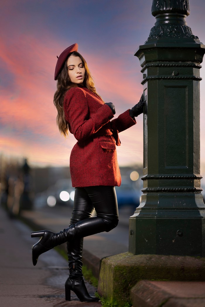 Woman wearing a red coat and beret posing by a lamppost