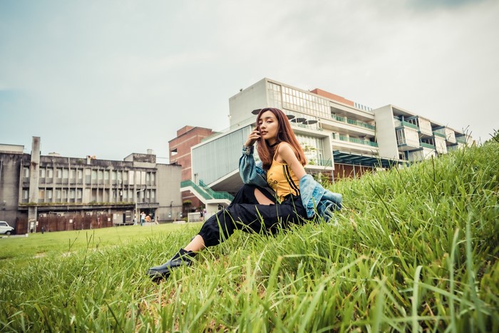 Asian woman sitting on grass in front of buildings