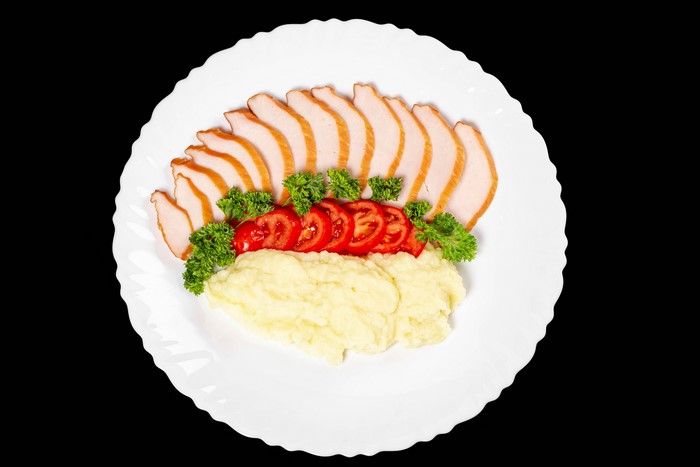 Sliced ham with mashed potatoes and tomatoes on a plate