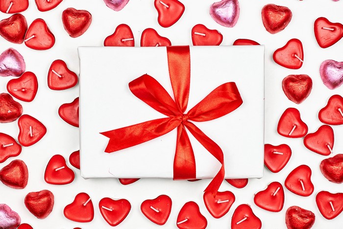 Gift box with red ribbon surrounded by heart-shaped candles