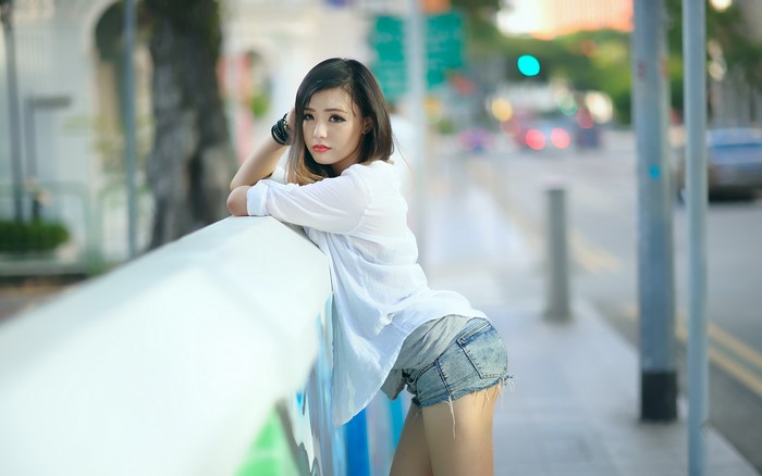 Asian woman in white shirt and denim shorts leaning on railing