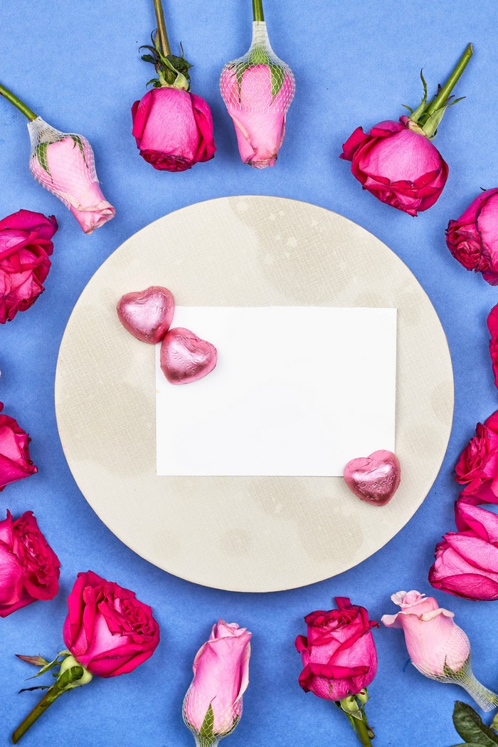Pink roses and heart candies on a blue background with a card