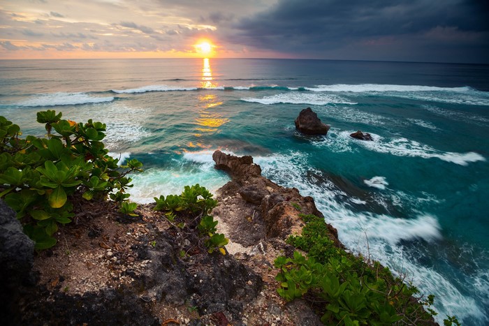 Sunset over the ocean with waves crashing on rocks