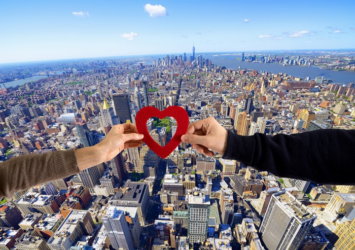 Hands holding a red heart over New York City