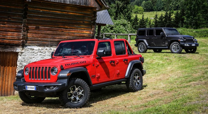 Two Jeep Wranglers, one red Rubicon and one black Sahara, parked near a wooden cabin