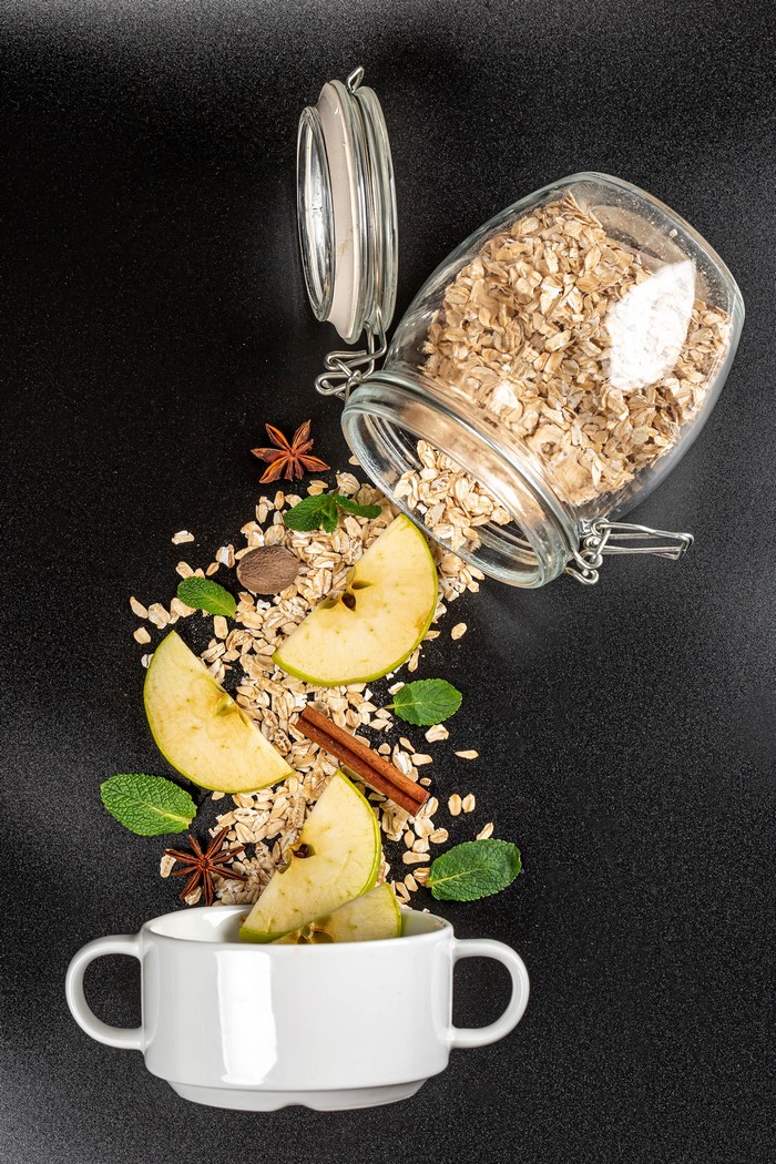Oatmeal with apples, cinnamon, and star anise spilling from a jar into a mug