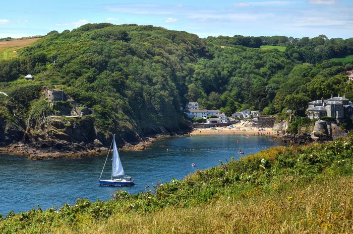 Sailboat in a bay with houses and a beach in Polruan, England