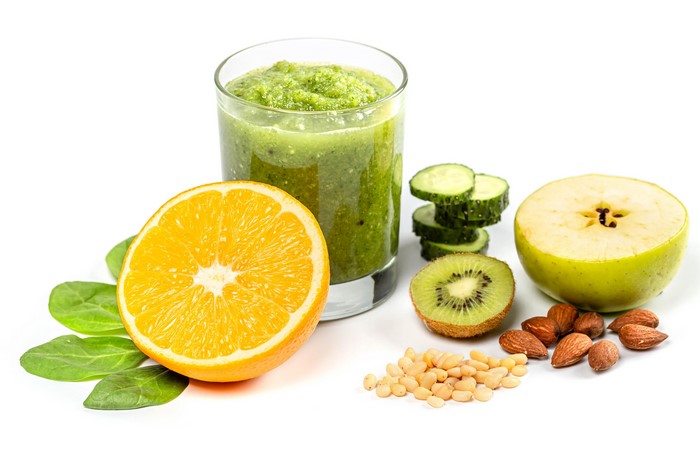 Green smoothie with orange, kiwi, apple, nuts, and spinach