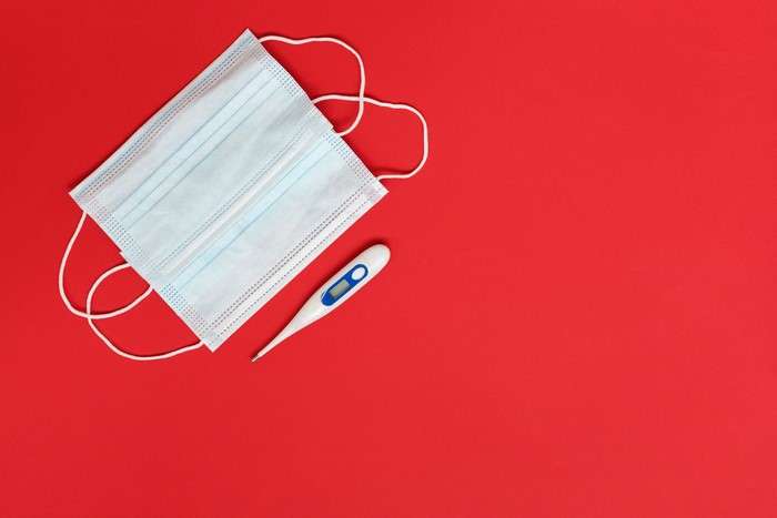 Face mask and thermometer on red background