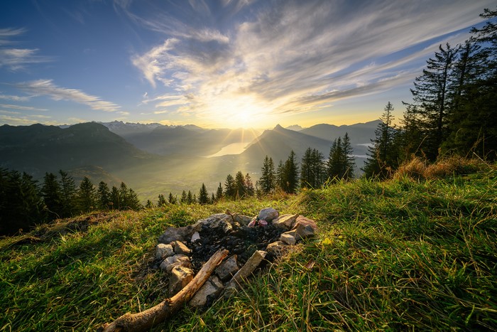 Campfire pit on a grassy mountain overlooking a lake at sunset