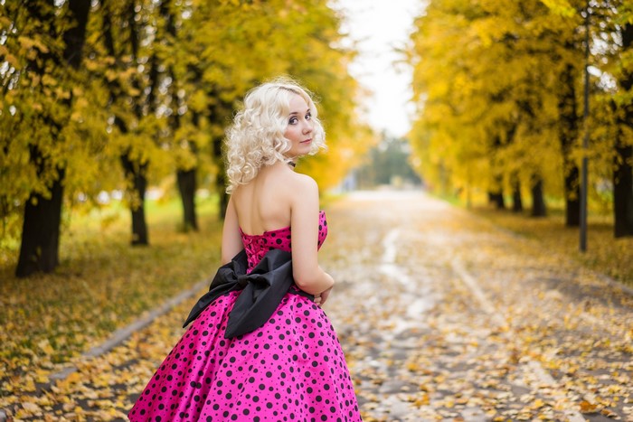 Blonde girl in a pink polka dot dress with a bowknot in autumn