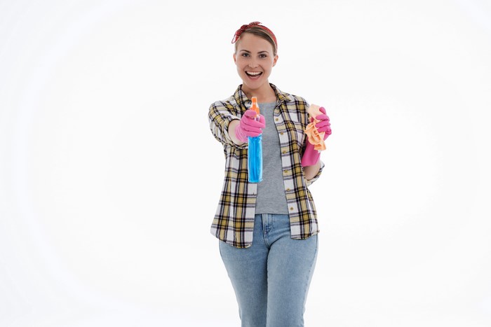 Woman in plaid shirt holding cleaning spray and cloth