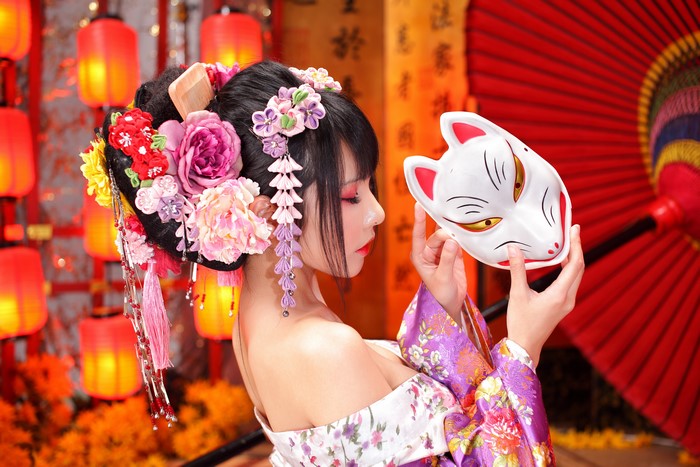 Woman in traditional Japanese attire holding a Kitsune mask