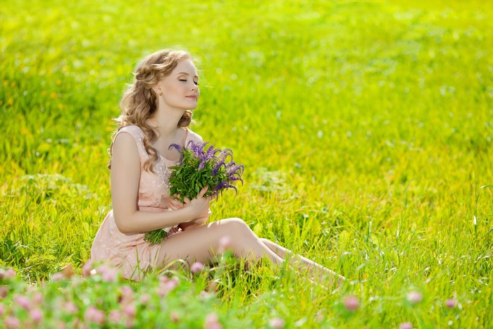 Blonde girl with bouquet sitting in grass