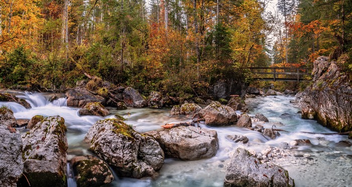 River flowing through autumn forest with wooden bridge in Germany