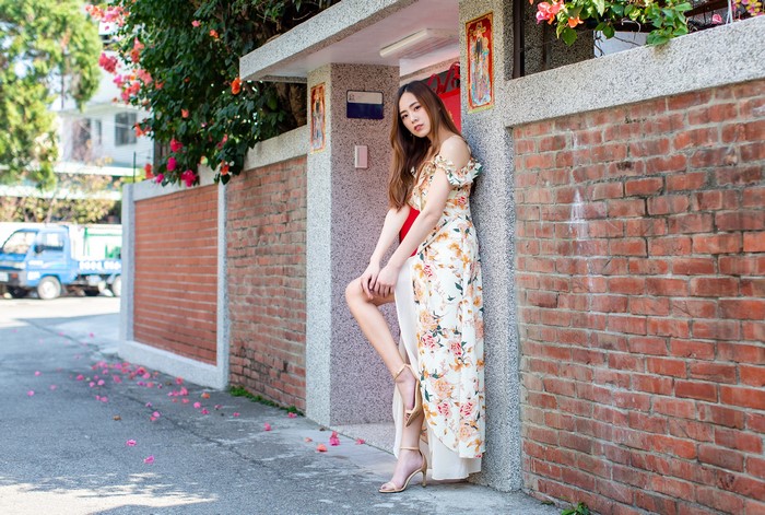 Woman in floral dress posing by brick wall