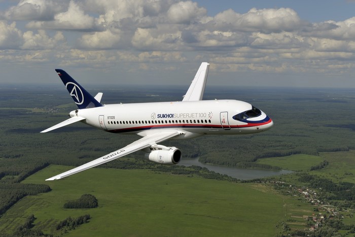 Sukhoi Superjet 100 airplane flying over green landscape