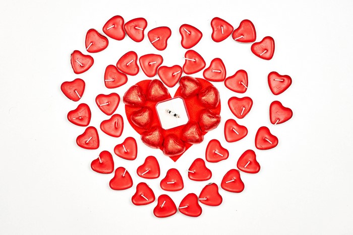 Heart shaped candles and ring on white background