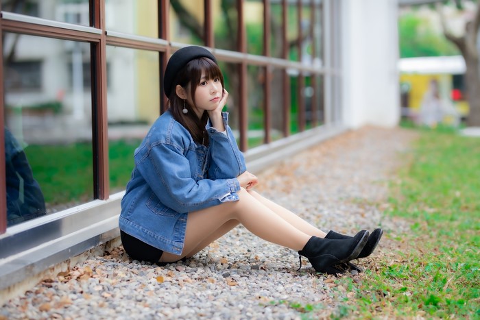 Asian girl in denim jacket and beret sitting outdoors