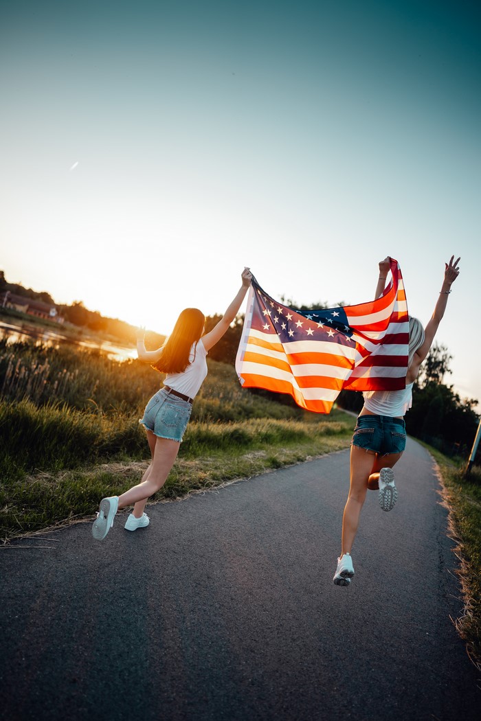Two girls running with American flag at sunset