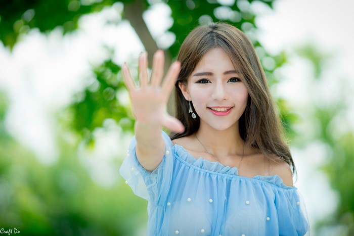 Asian woman with brown hair smiling and holding up hand