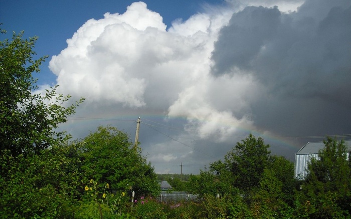Rainbow over a rural landscape with trees and clouds