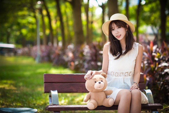 Asian girl with teddy bear on a park bench
