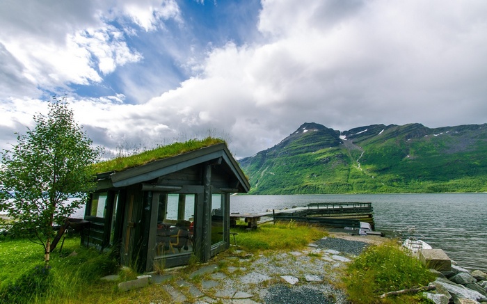 Cabin with grass roof by a lake and mountains