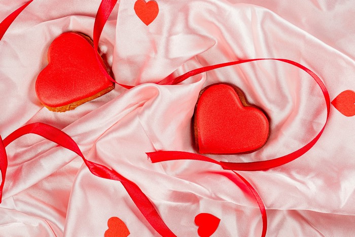 Two heart-shaped cookies with red ribbon on pink satin