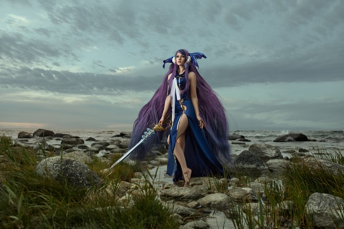 Cosplayer with purple hair and sword on rocky shore