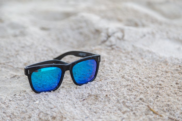 Black sunglasses with blue lenses on sand