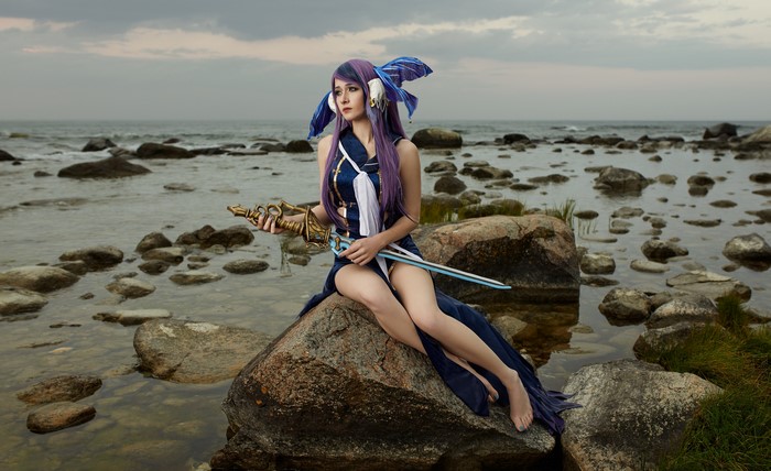 Cosplayer with sword sitting on rocks by the sea