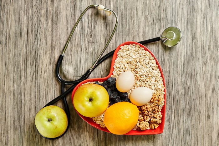 Heart-shaped bowl of oatmeal with fruits, eggs, nuts, and stethoscope