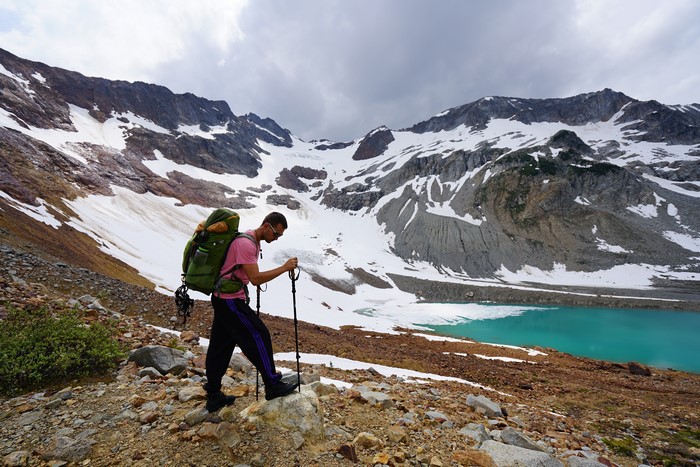 Man with backpack hiking near snowy mountains and lake