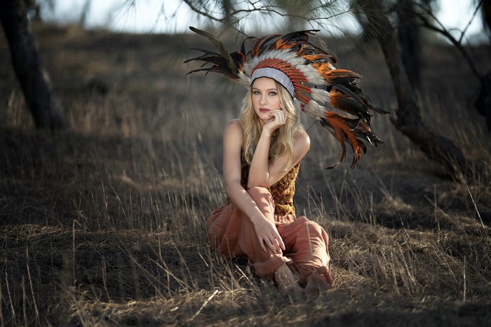 Blonde girl with war bonnet sitting in dry grass
