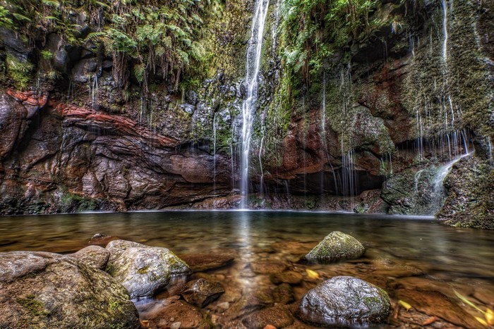 Waterfall cascading over mossy rocks into a clear pool in Madeira, Portugal