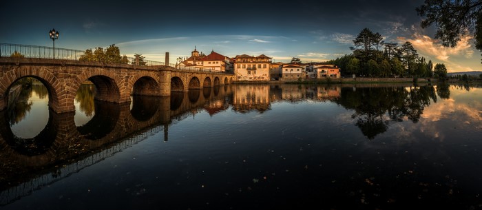 Stone bridge over river with houses and trees, Portugal
